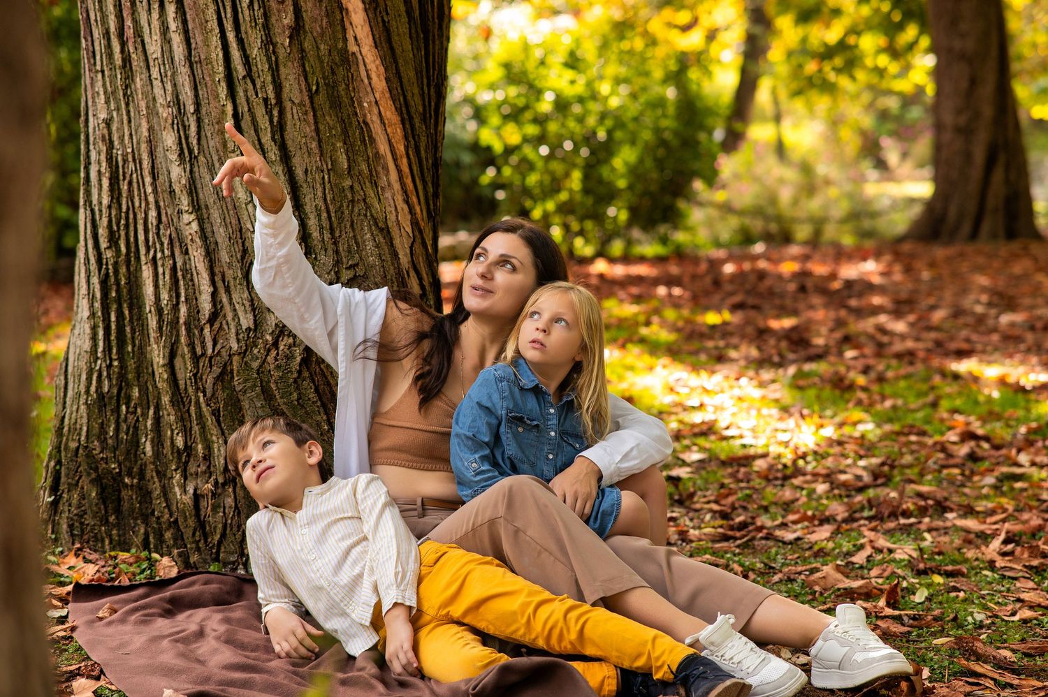 People lying on autumn leaves in a park during golden hour as sunlight filters through trees.