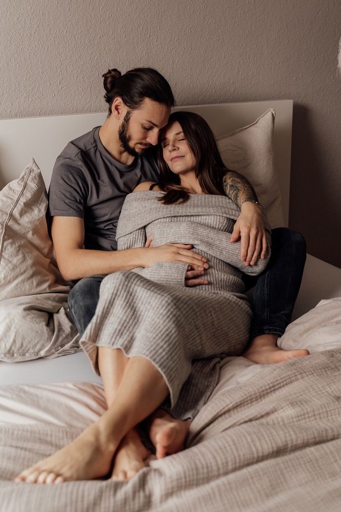 A couple shares an intimate moment while lying together on a gray bed with textured bedding.