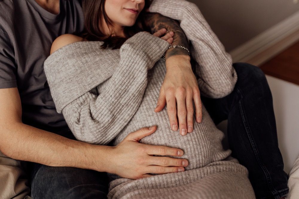 A couple sits close together on a couch wearing casual sweaters in an intimate moment at home.