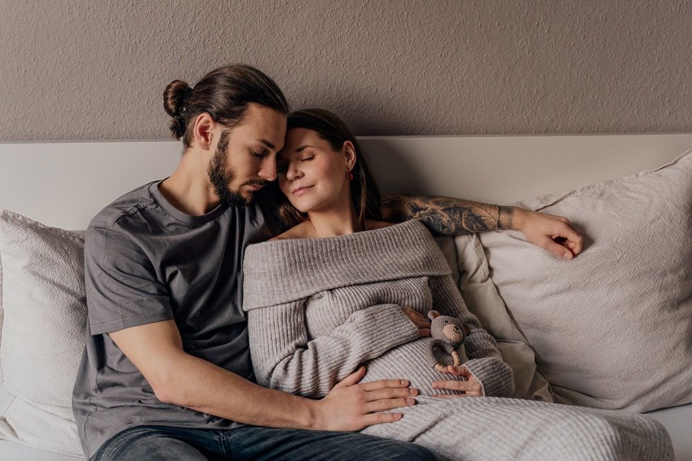 A couple lies together intimately on a grey couch, sharing tender moments in a sequence of romantic poses.