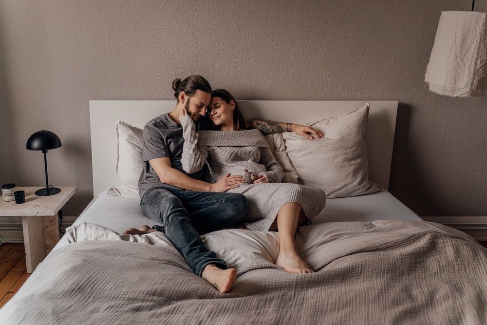 People relaxing together in a cozy bed with gray bedding and white pillows.