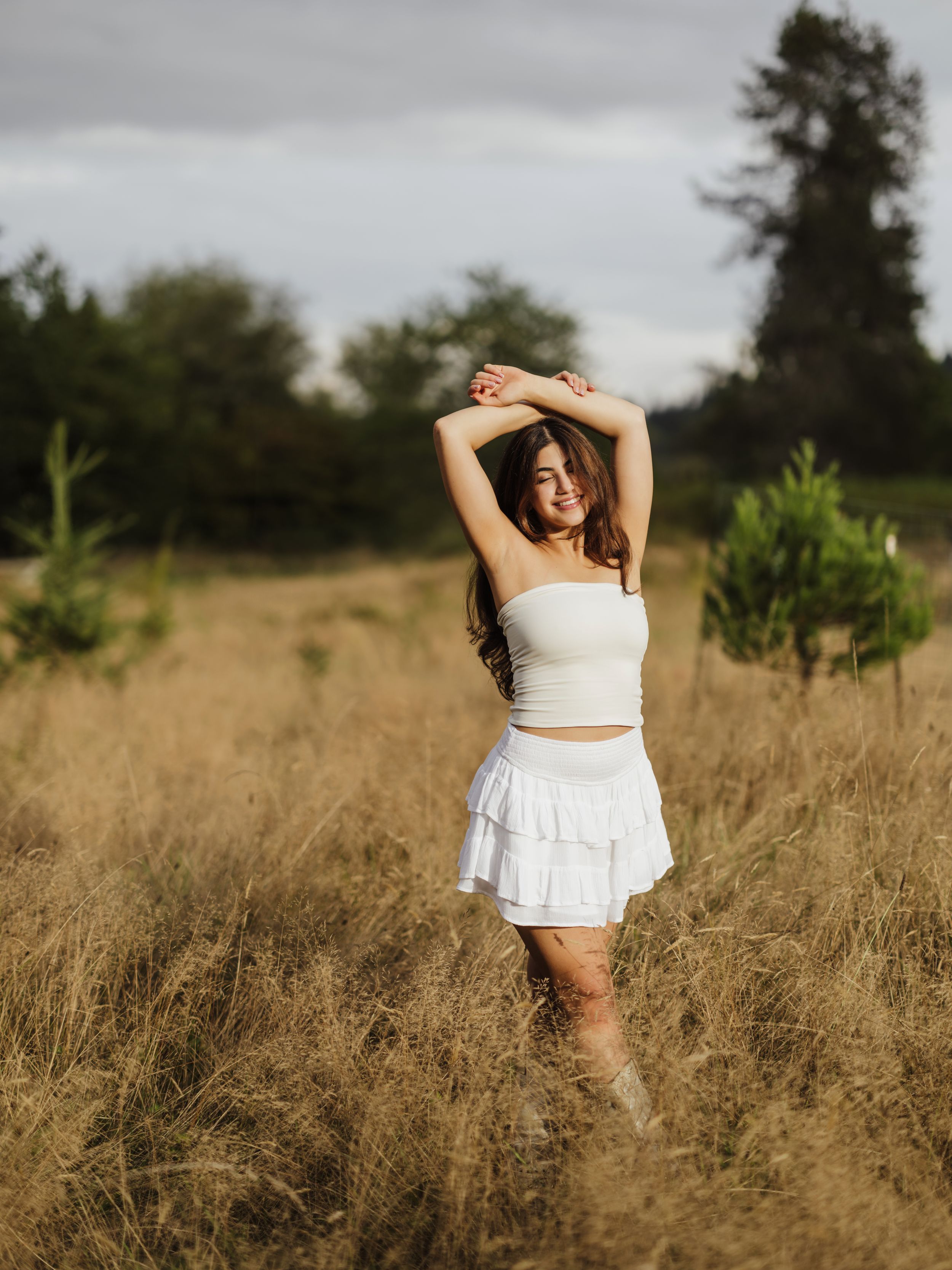 A person in a white dress twirls joyfully in a golden wheat field during sunset.