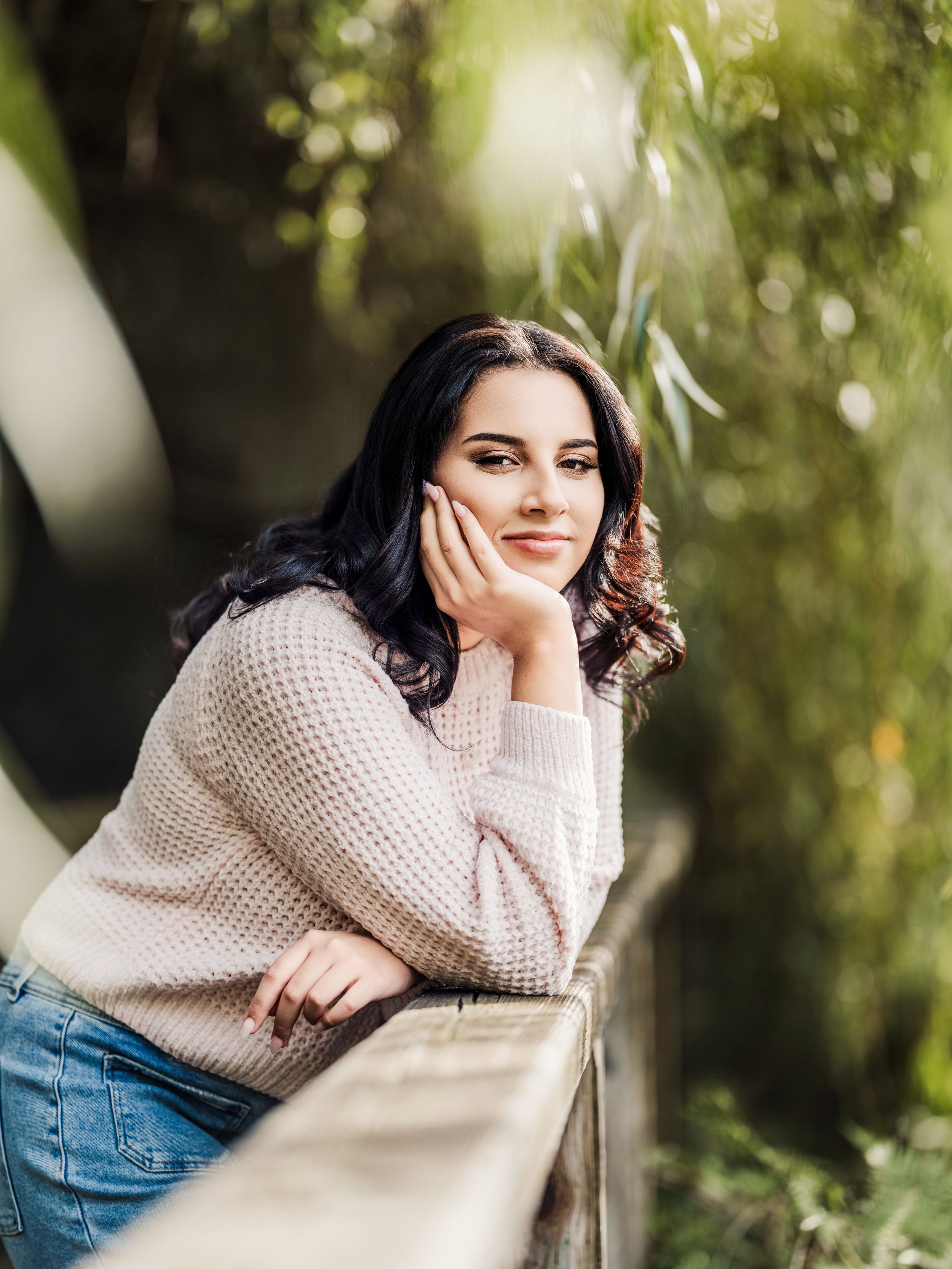 A person in a cozy beige sweater poses against a soft natural background with bokeh lighting effects.