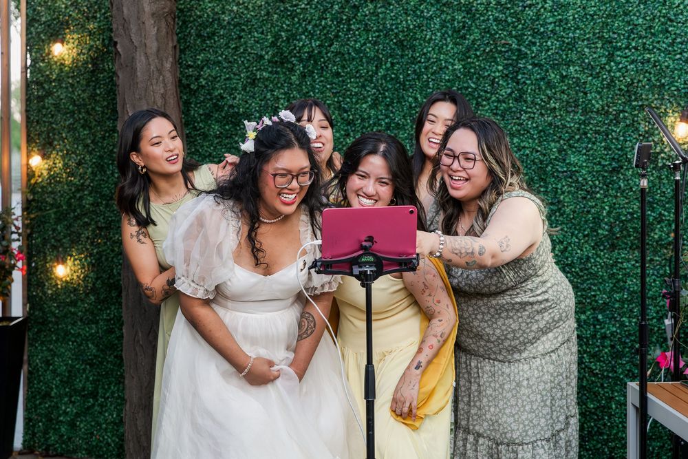 Wedding guests posing with bride against lush green hedge wall with string lights at Wilcox Gastropub in Mississauga, Ontario.