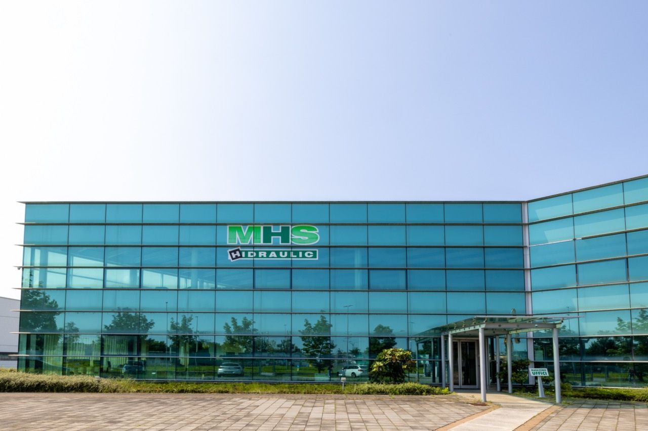 Modern glass office building with MBS Corporate logo on exterior facade reflects blue sky and landscaping.