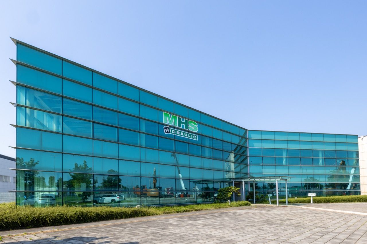 Exterior view of a modern glass office building with blue-tinted windows and curved architectural design.