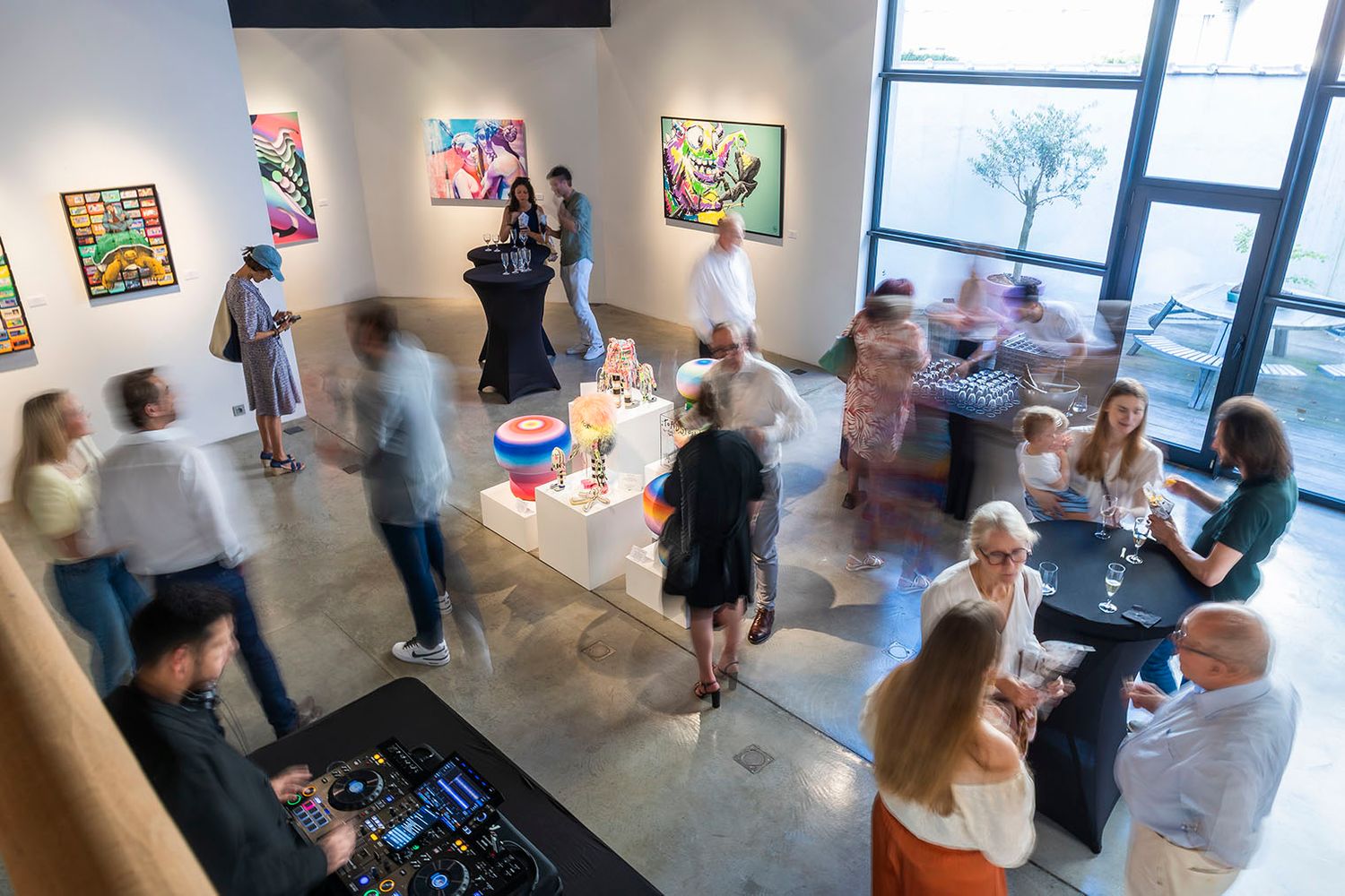 Art gallery visitors admiring colorful artwork displayed on white walls during an exhibition opening.