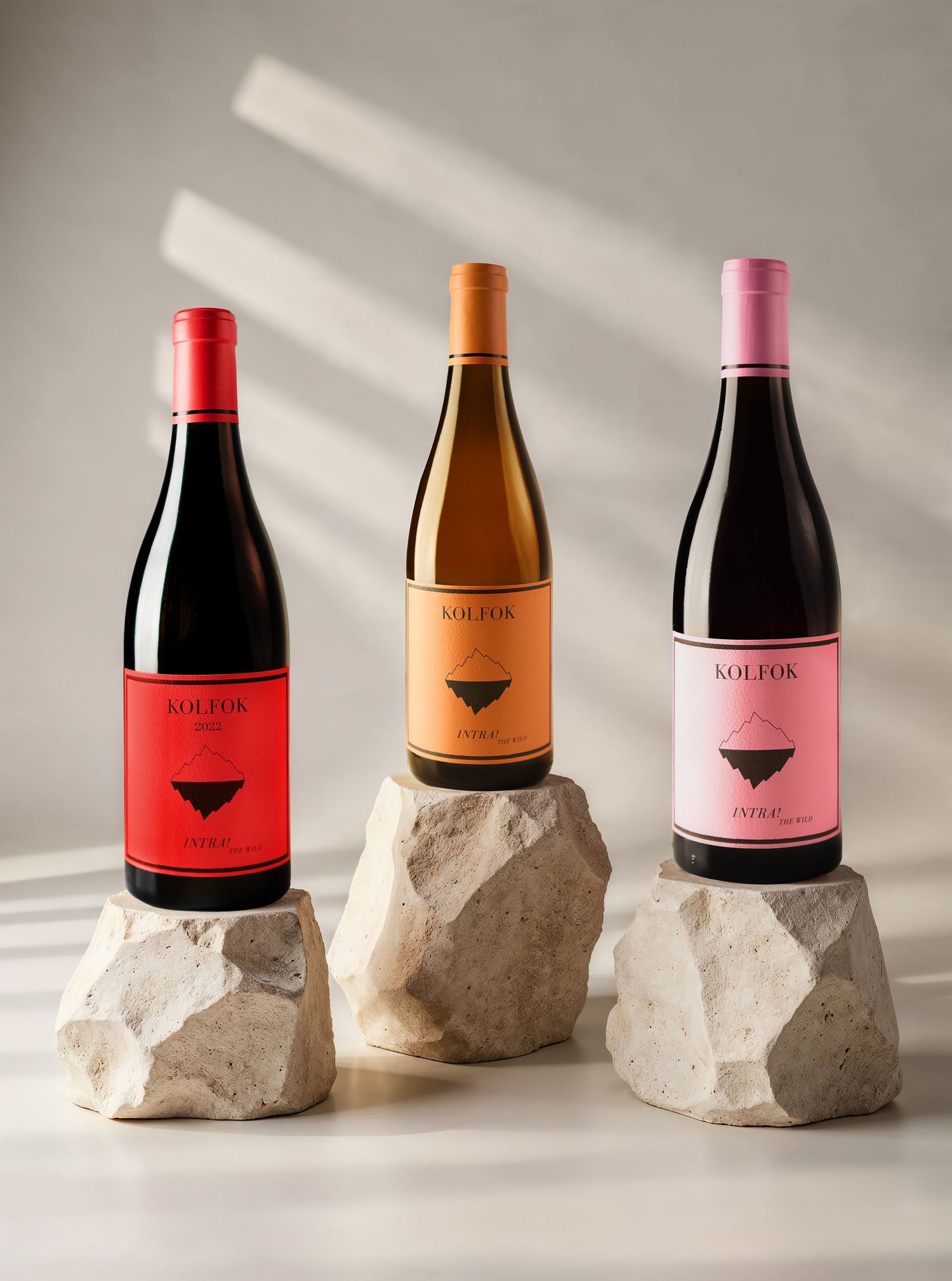Three Kolfok wine bottles balanced on natural stone rocks in soft natural light.