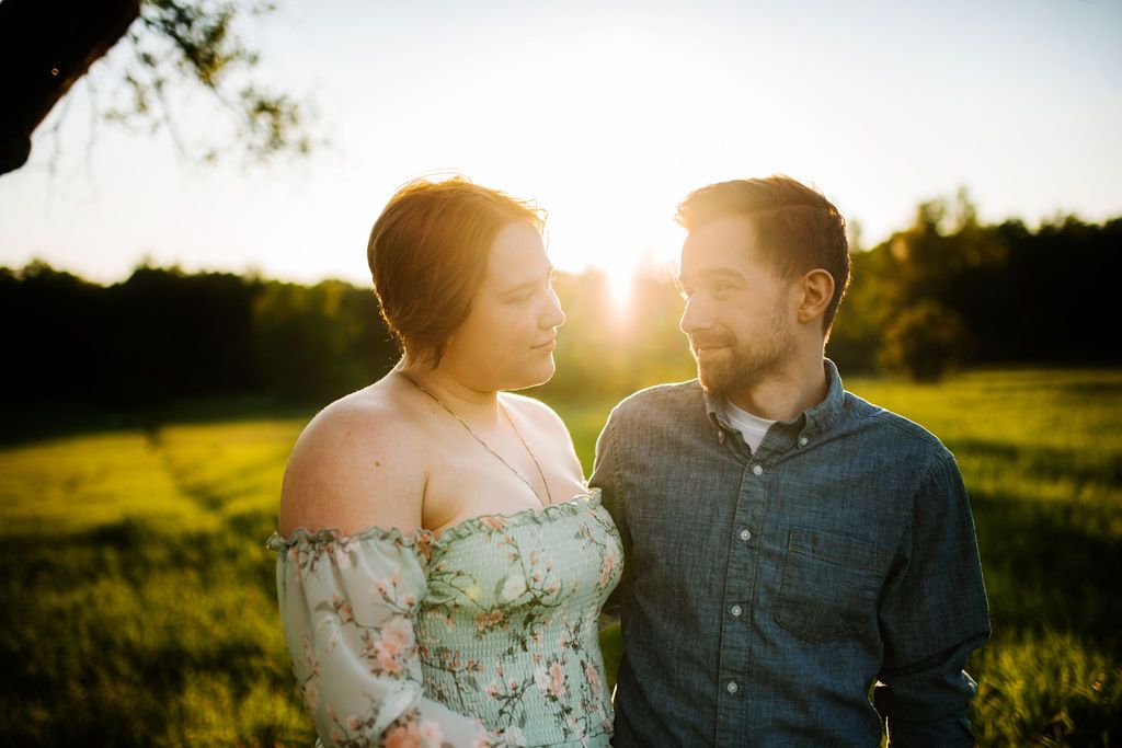 Romantic engagement photos at sunset in a golden field with soft backlighting.
