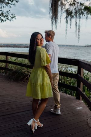 Couple shares romantic moments on a wooden boardwalk overlooking a serene waterfront.