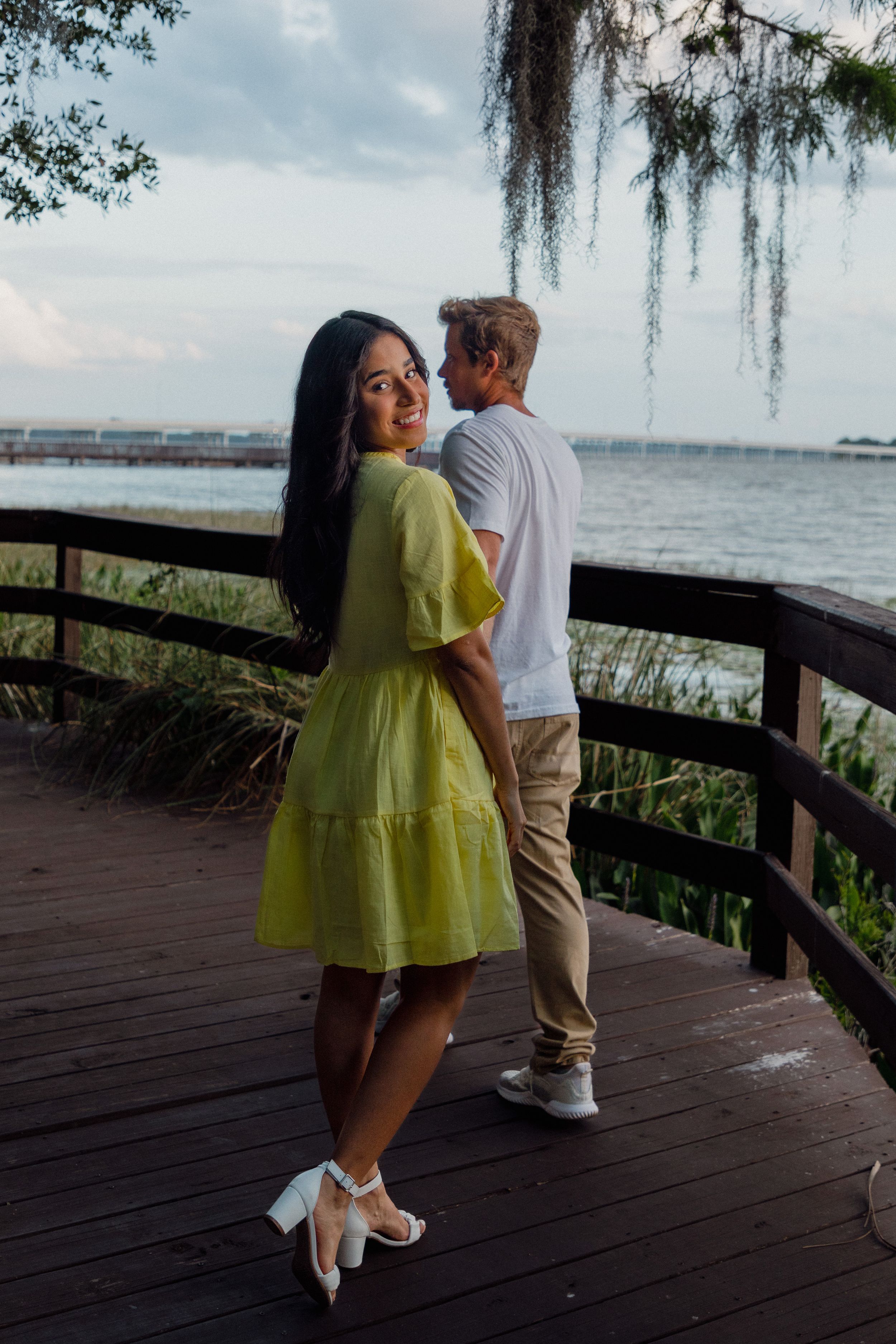 Couple shares romantic moments on a wooden boardwalk overlooking a serene waterfront.