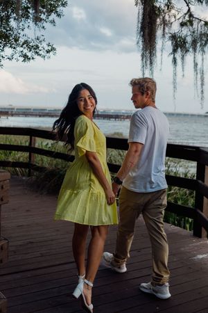 A couple shares a romantic moment on a wooden boardwalk overlooking the water with Spanish moss hanging overhead.