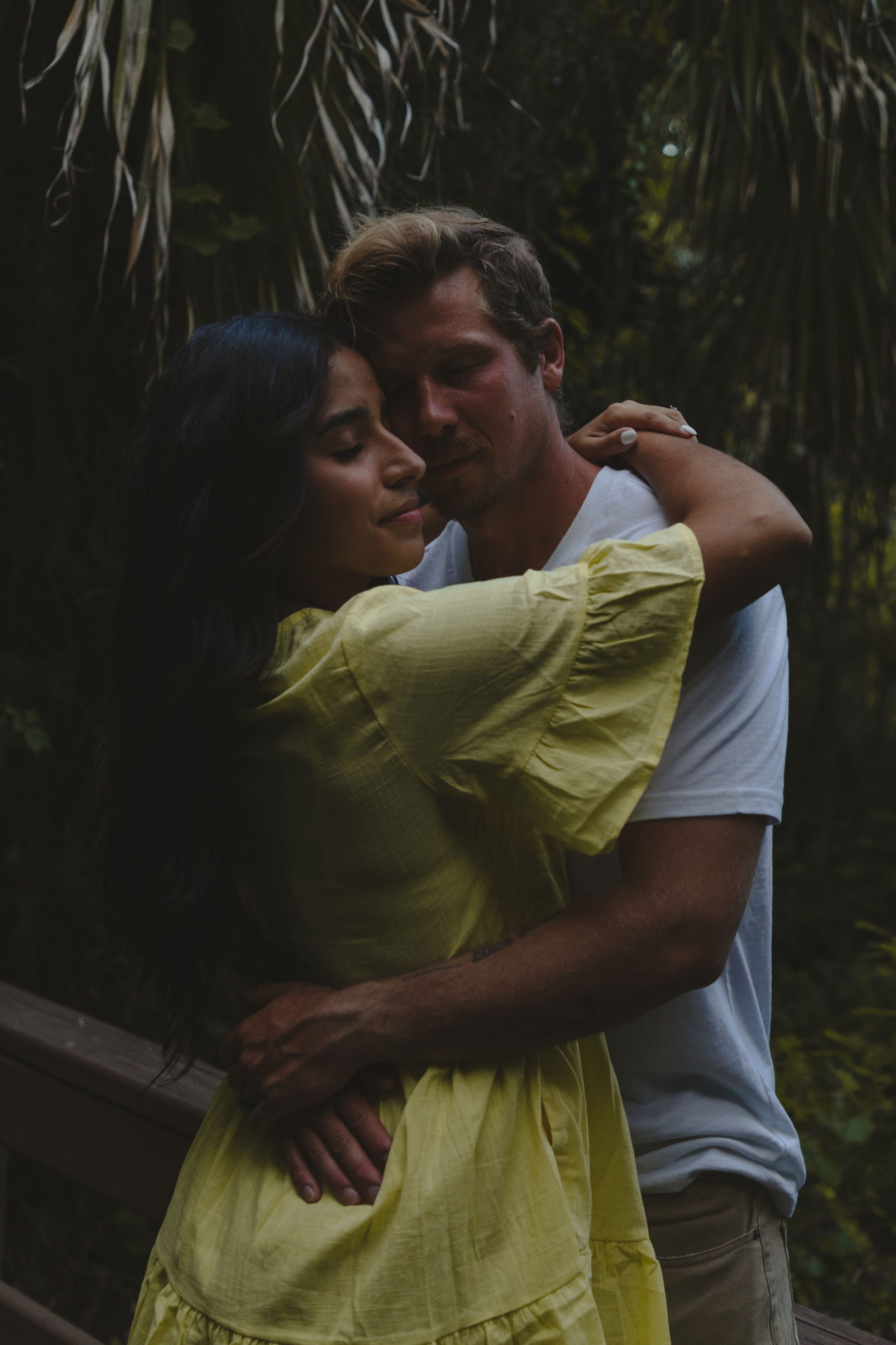 Romantic couple embraces in a garden setting with lush greenery in the background.