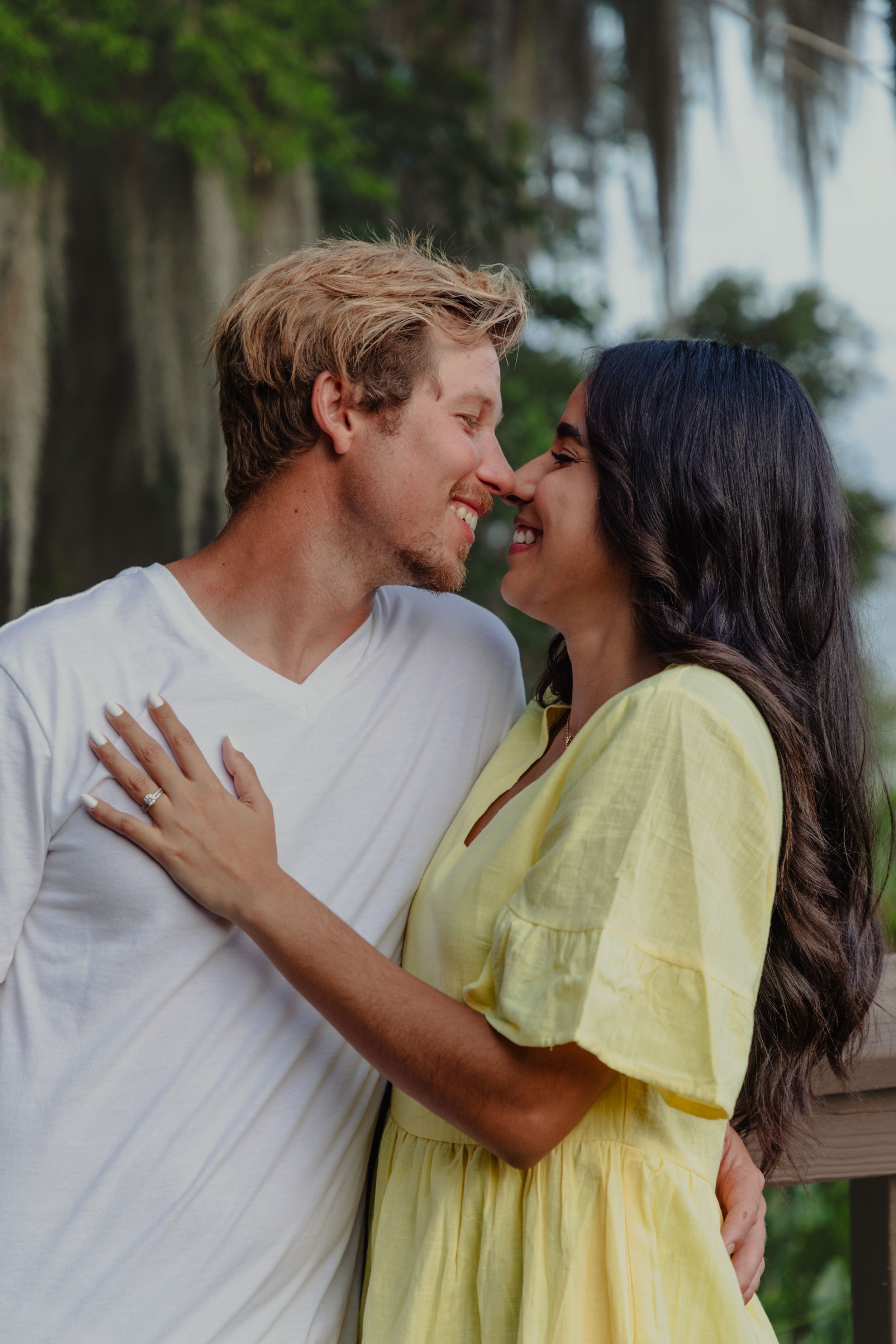 Intimate couple shares tender moments while wearing yellow and white against a natural backdrop.