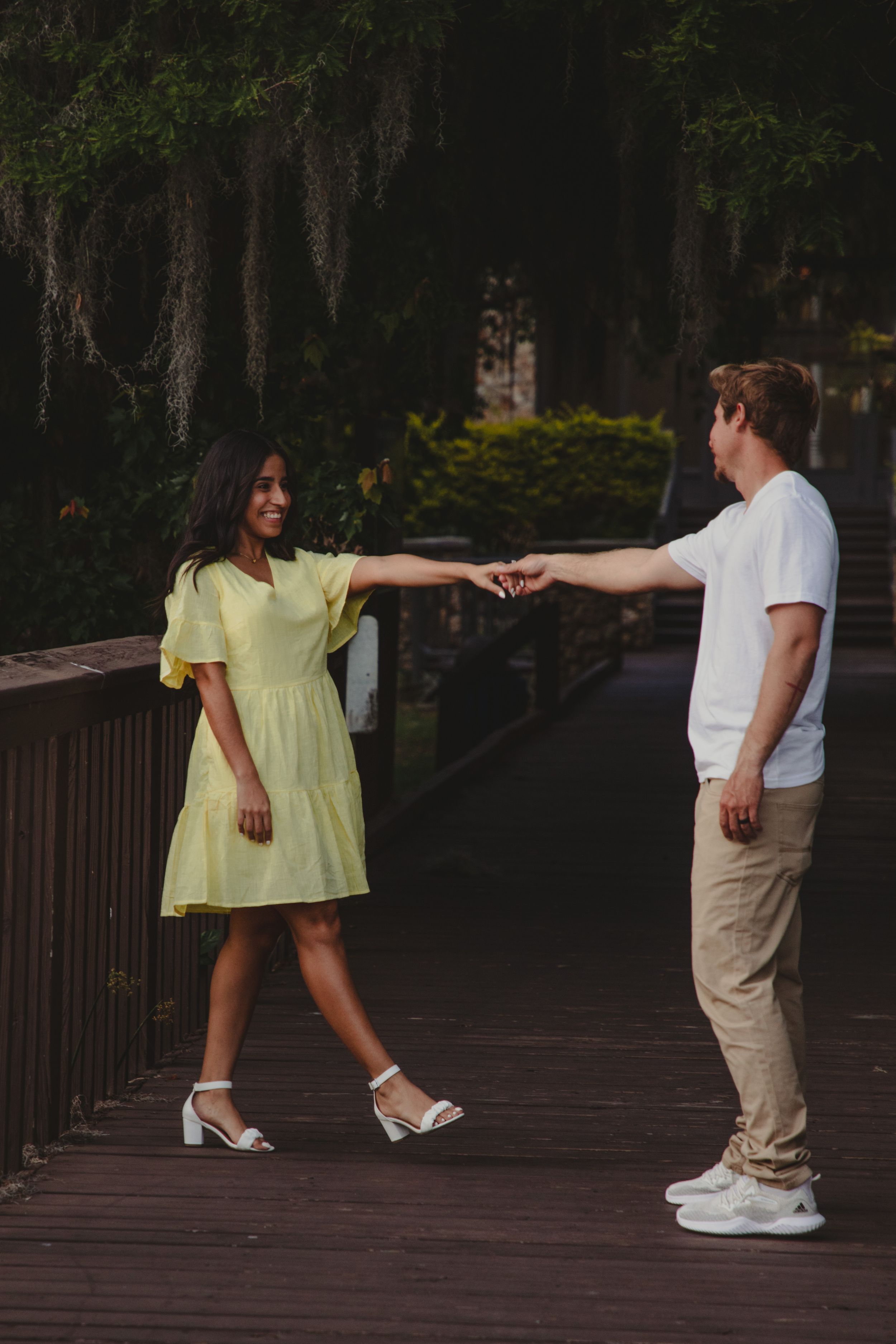 A couple walking together on a wooden boardwalk in a forest setting during sunset.