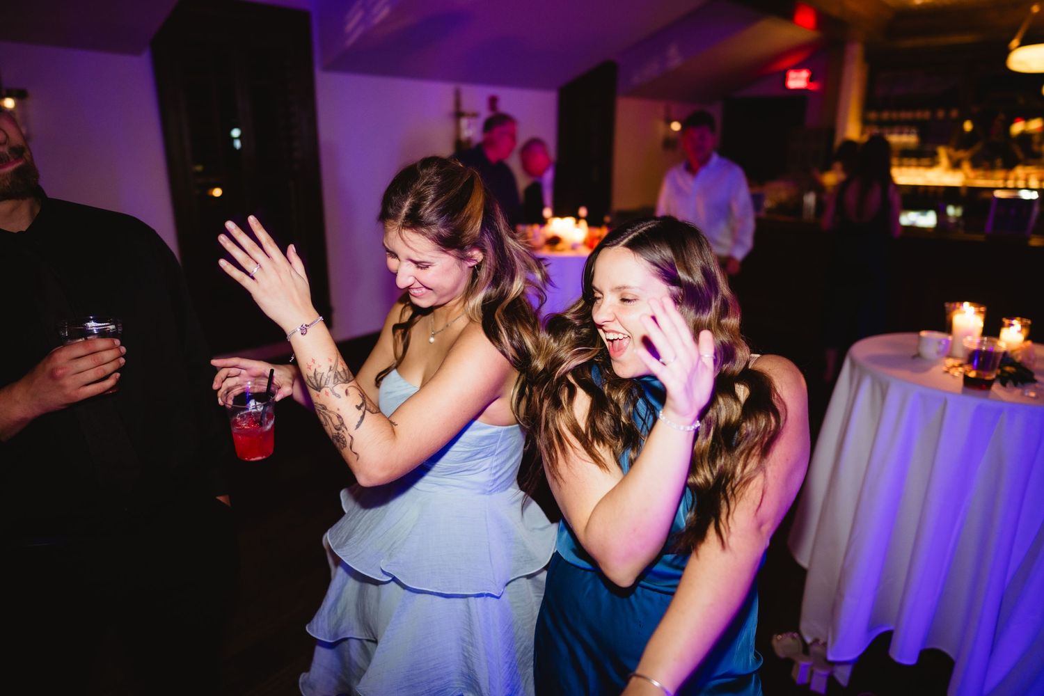 People dancing and celebrating at a dimly lit nightclub or party venue with colorful purple lighting effects.