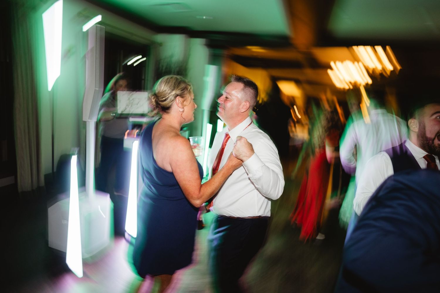 People dancing at a wedding reception with motion blur and green lighting effects in a dark venue.