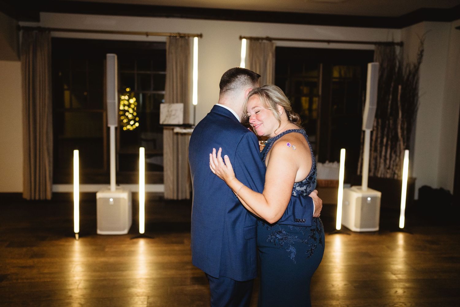A couple dances together in a dimly lit ballroom during an intimate slow dance moment.