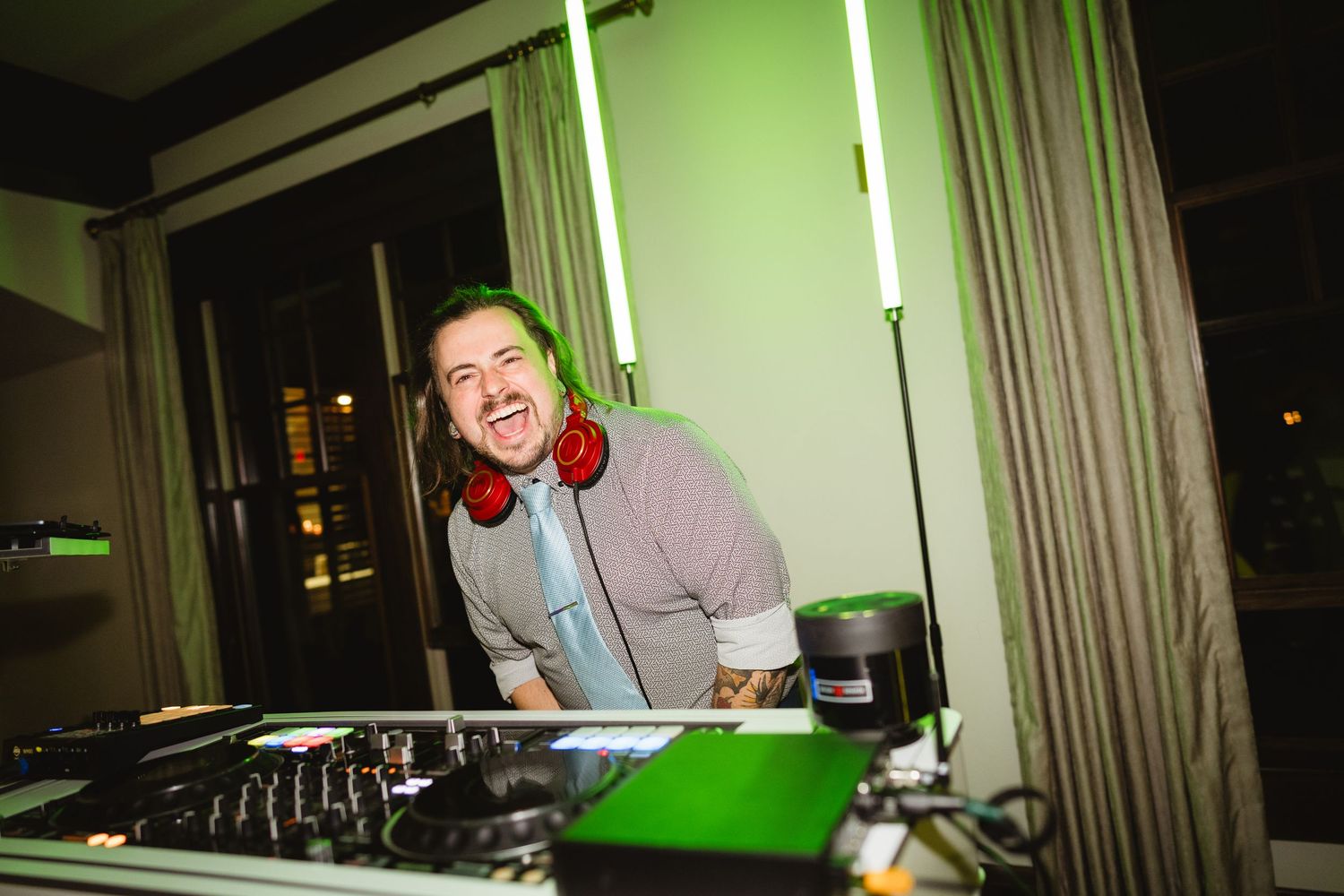 DJ performs at a nightclub with red headphones and mixing equipment under green lighting.
