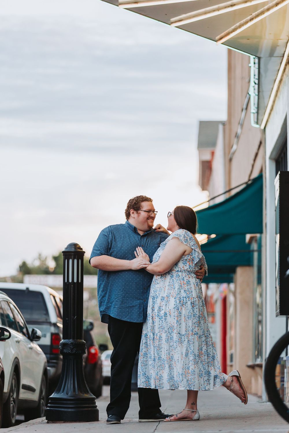 A couple in casual attire shares an intimate moment outside a storefront with green awnings.