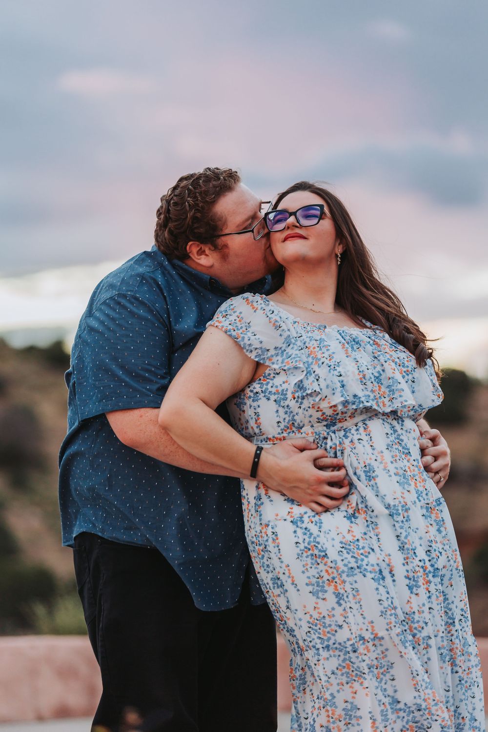 A romantic couple embraces outdoors at sunset, with the person in a floral dress smiling joyfully.