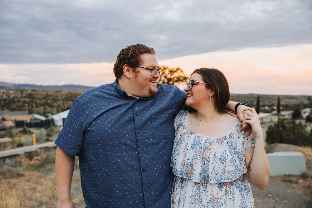 A couple in coordinating blue outfits share romantic moments together during a sunset photoshoot in a desert landscape.