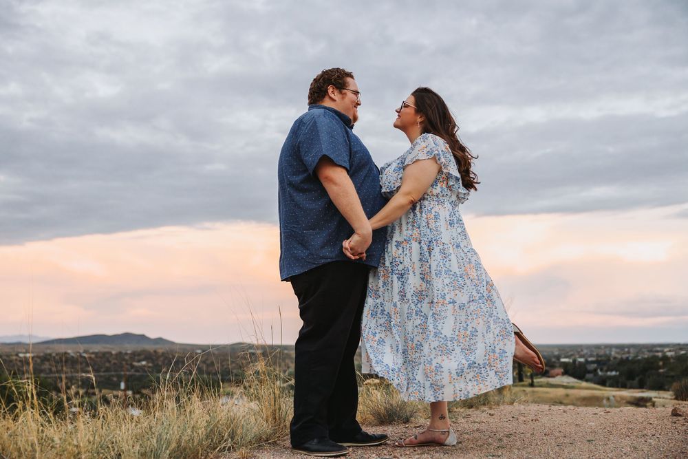 A couple shares a tender moment against a cloudy sky during a romantic outdoor photoshoot.