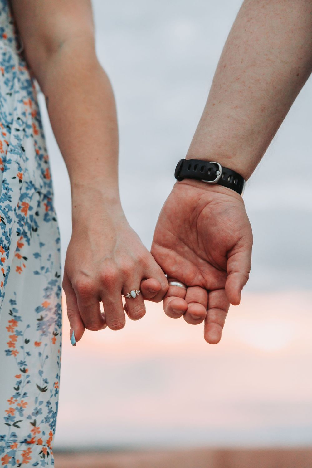 Close-up view of two hands holding each other against a blurred background with floral pattern.