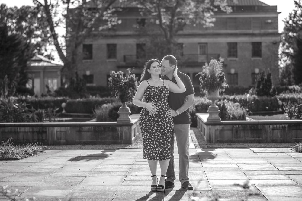 A couple dances together on an outdoor stone patio with classic buildings in the background.