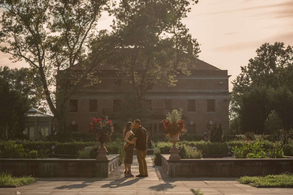 Silhouettes of people walking along a path at sunset with buildings in the background.