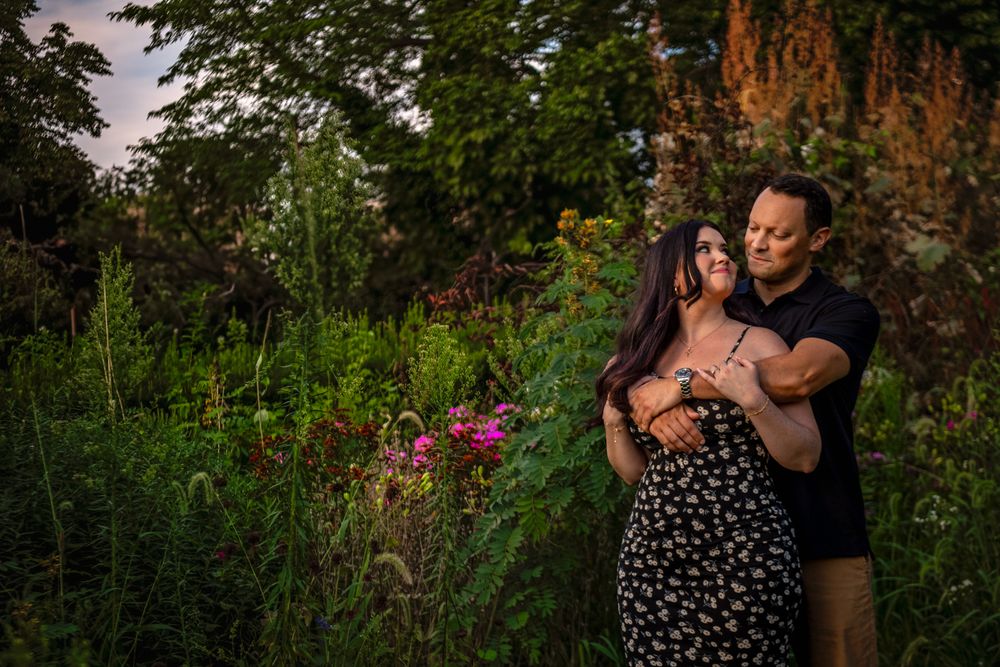 Couple embracing outdoors in a romantic garden setting with lush greenery and trees.