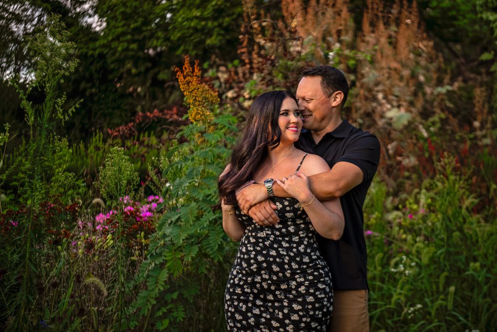 A couple embraces in a lush garden with wildflowers and natural greenery surrounding them.