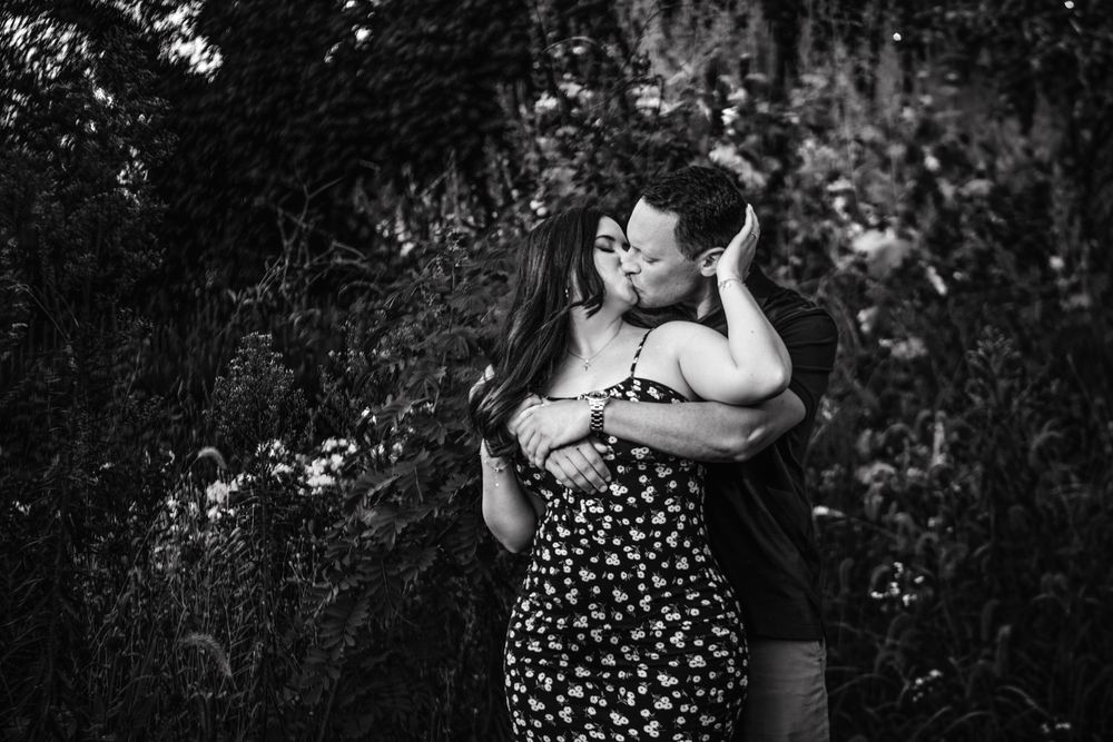 A romantic black and white portrait of a couple embracing in a garden setting.