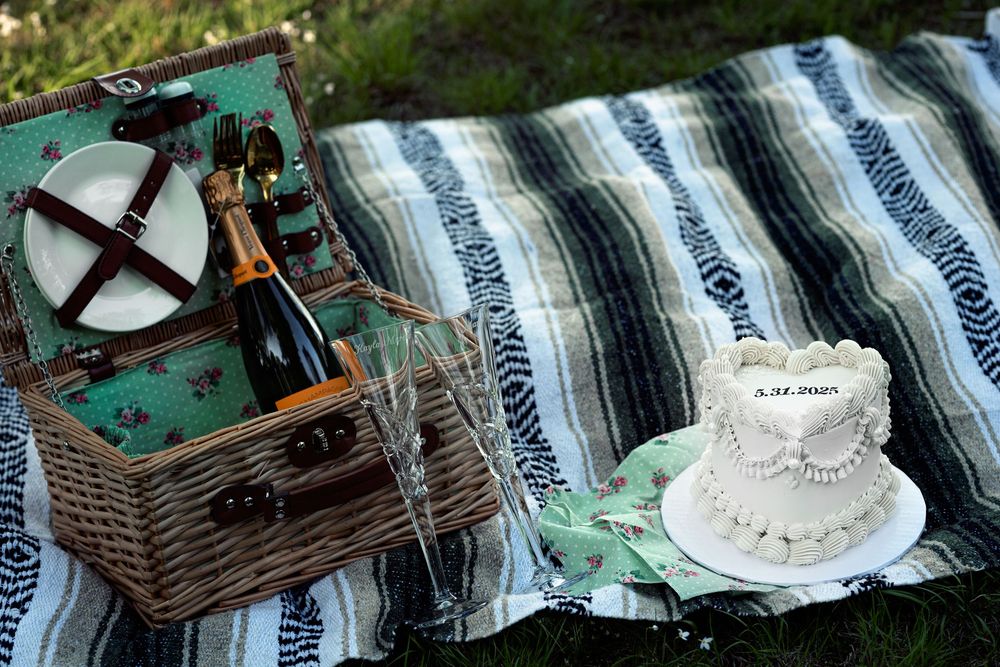 A vintage picnic setup with a wicker basket and teacup on a striped blanket in an outdoor setting.