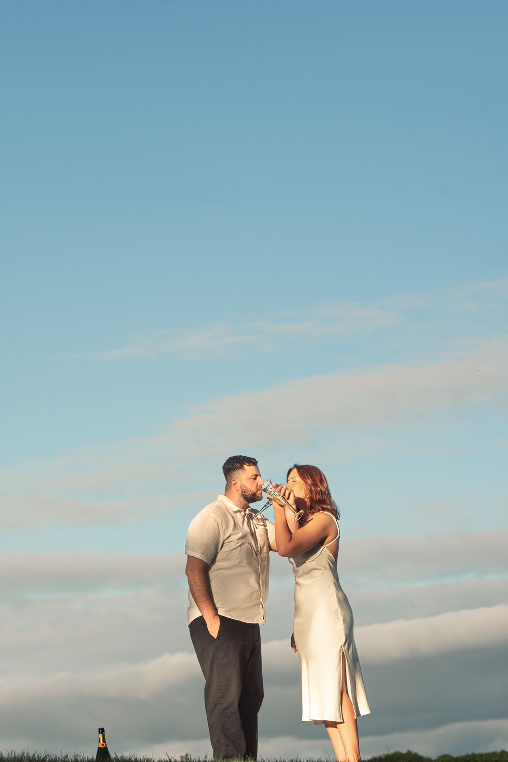 Couple sharing an intimate moment against a bright blue sky with wispy clouds at sunset.