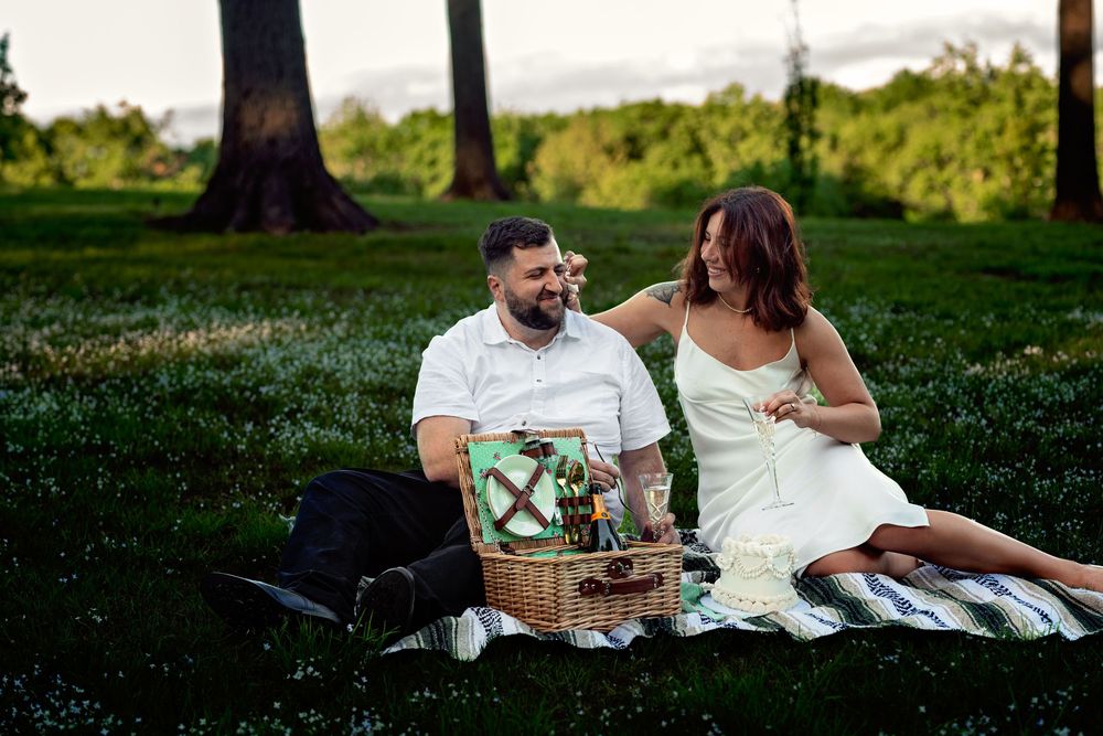 Couple enjoying a romantic picnic on a grassy hillside during golden hour with wine and snacks.