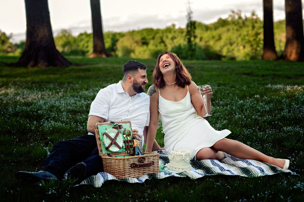 Couple enjoying a romantic picnic on a grassy hill during golden hour with wine and snacks.