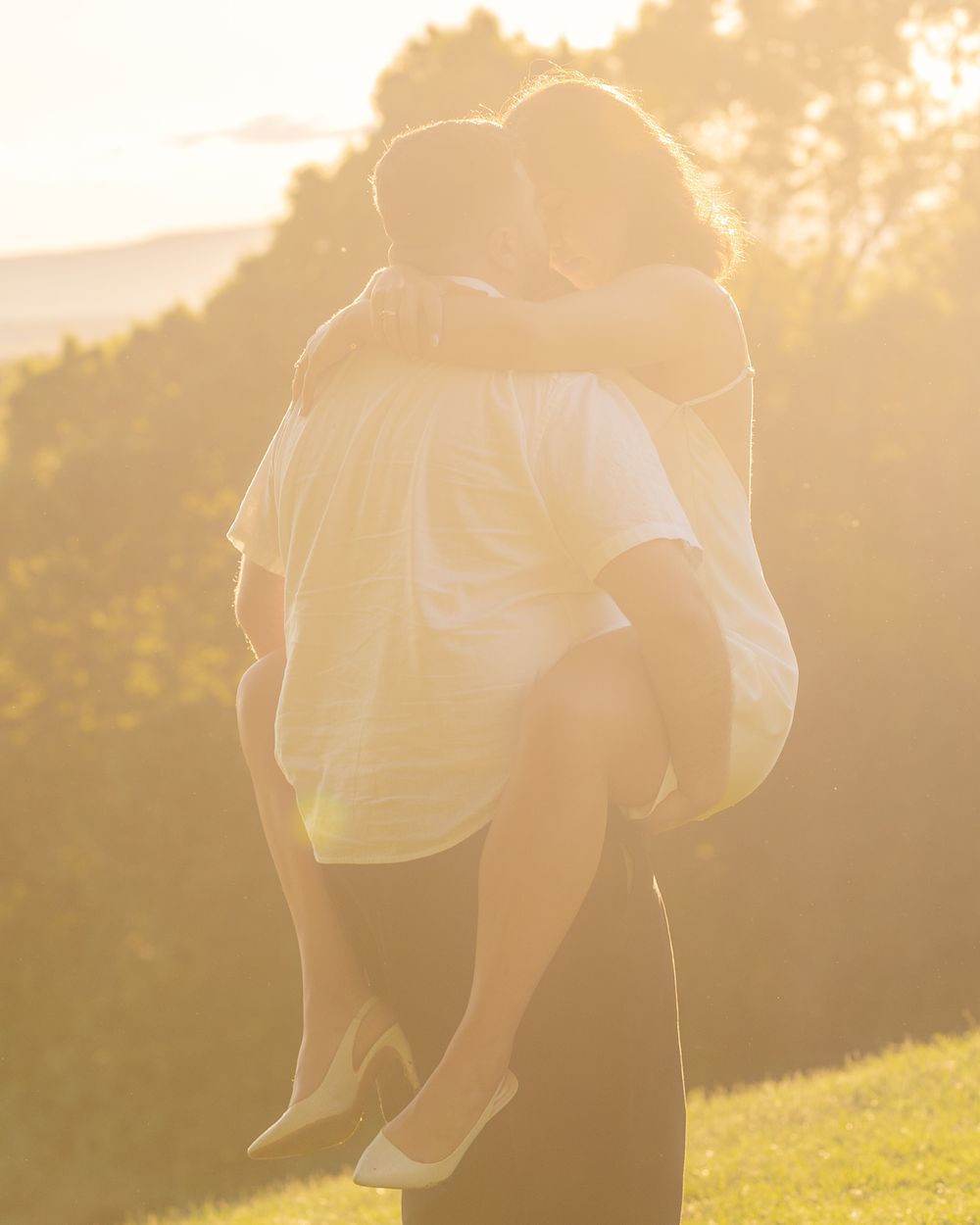 A couple embraces in a sunlit meadow during golden hour, creating a romantic silhouette against the warm sky.