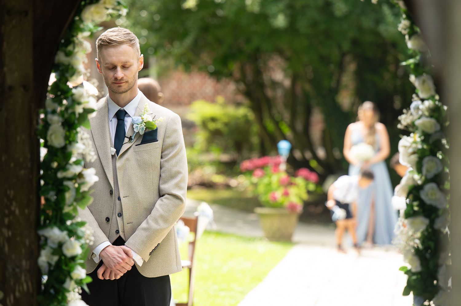Groom in suit waiting at Solton Manor ceremony, bridesmaids walking up aisle in Godric’s Garden, captured by SHOT by JFK.