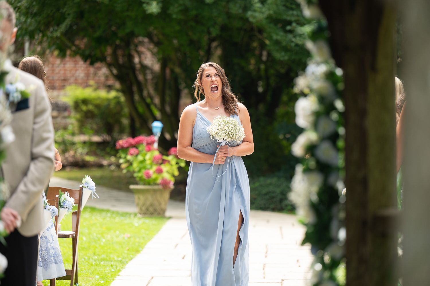 Candid moment at Solton Manor wedding as bridesmaid laughs and shouts excitedly toward the groom during ceremony.