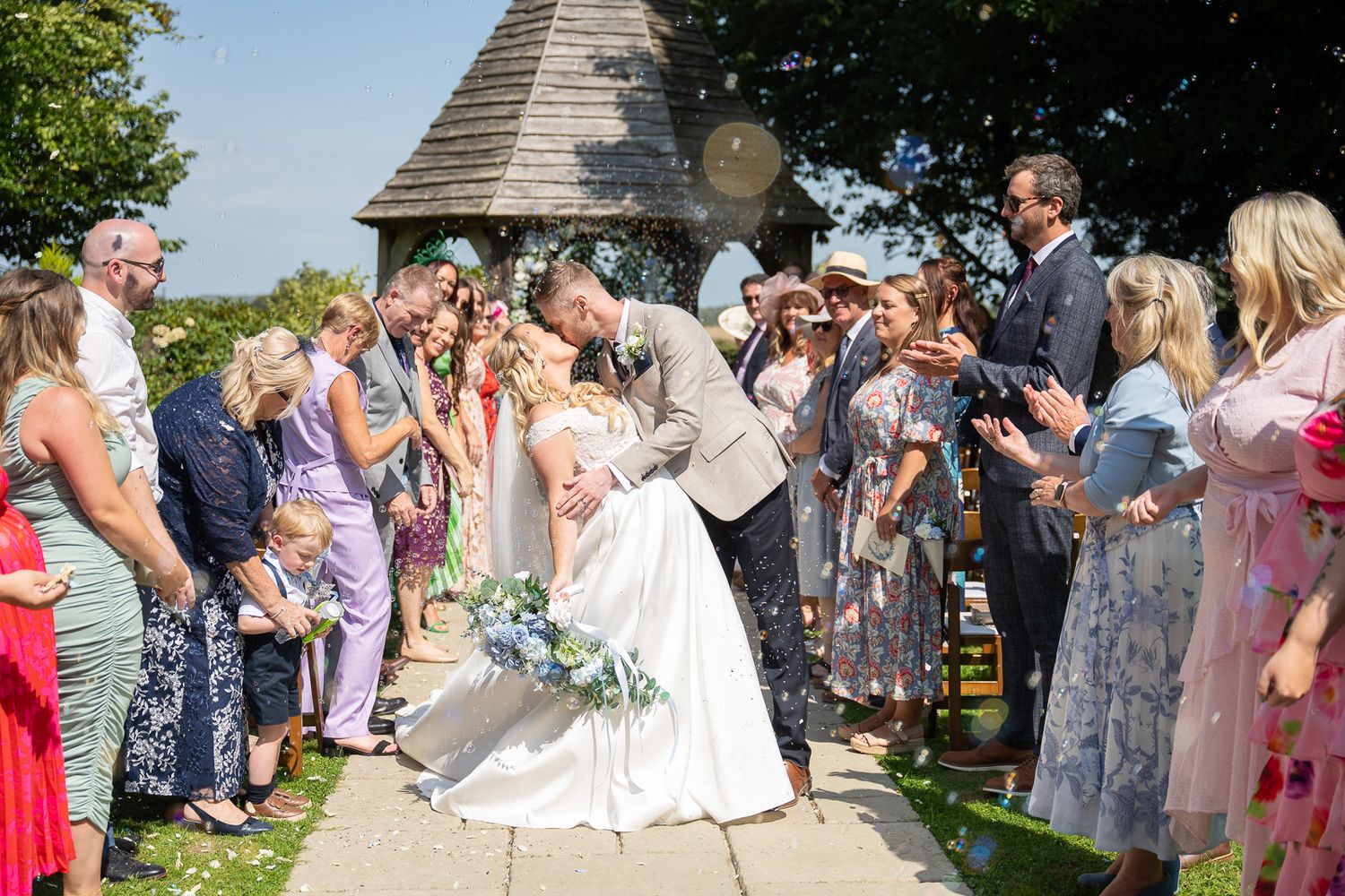 Confetti and bubbles fill the air as groom dips bride for a kiss at sunny Solton Manor wedding, Kent photographer SHOT by JFK Photography.