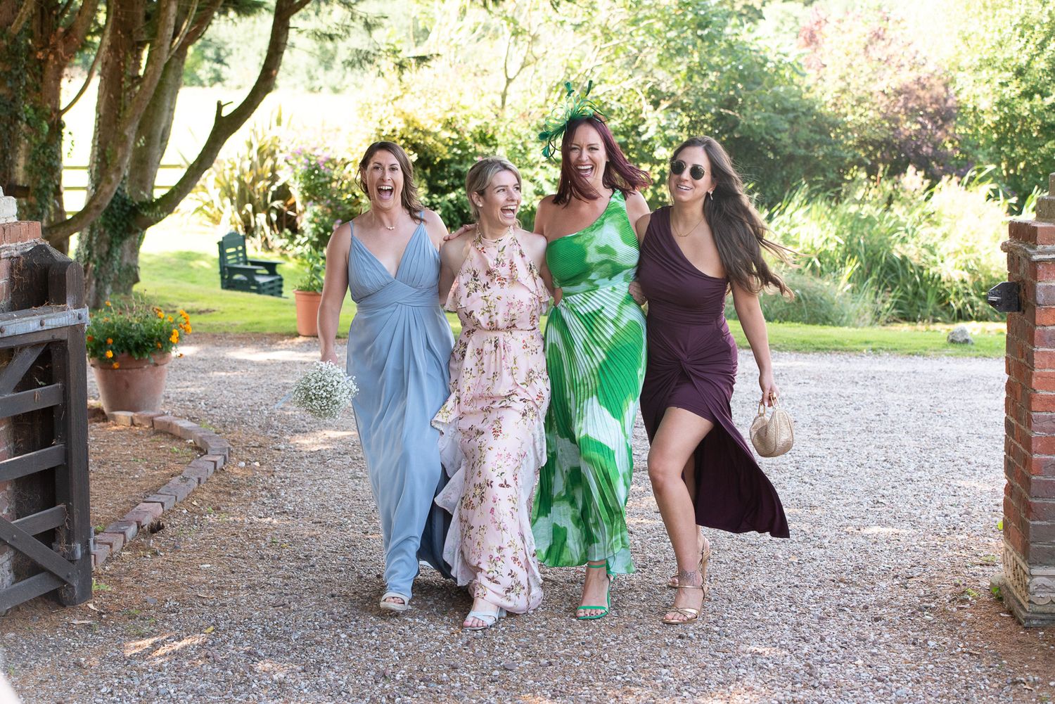 A group walks together and laughs on a gravel path surrounded by lush greenery on a sunny day.