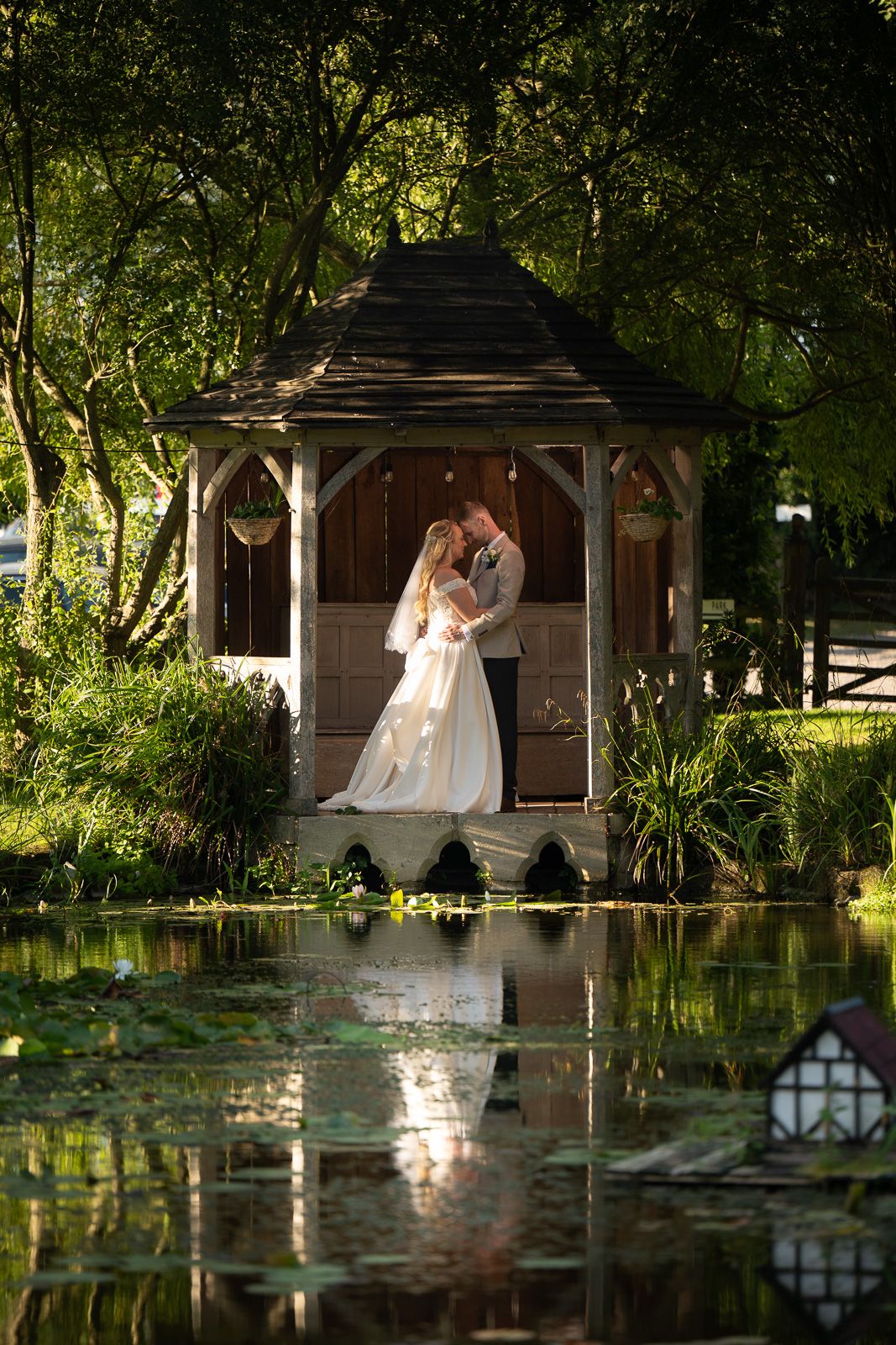 Bride and groom in The Summer House at Solton Manor, reflected in pond lilies under golden evening light.