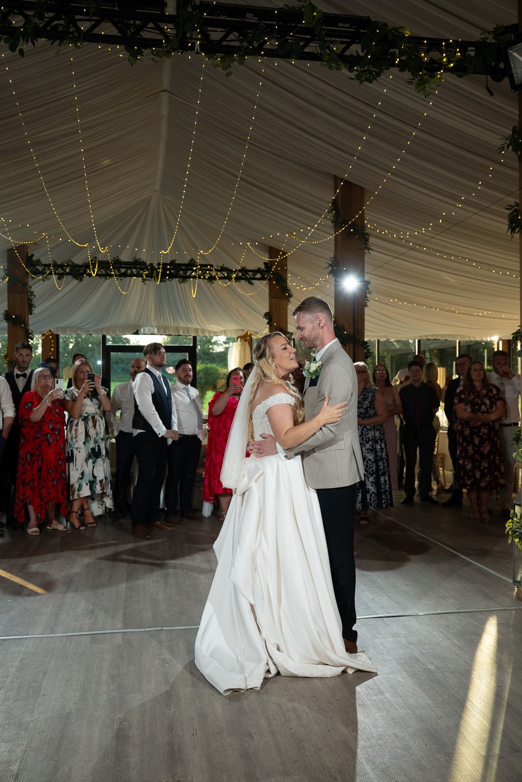 A sequence of photos showing a couple dancing their first dance at a wedding reception under a white tent with string lights.