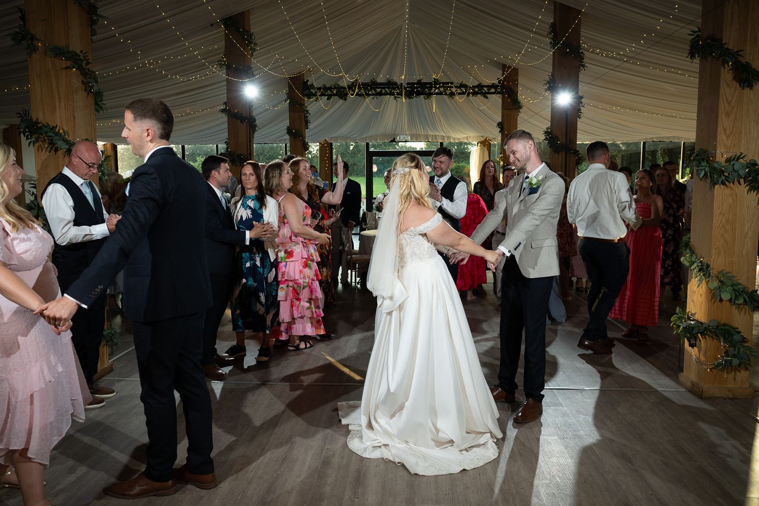 Wedding reception dance in a rustic barn venue decorated with greenery and twinkling lights.