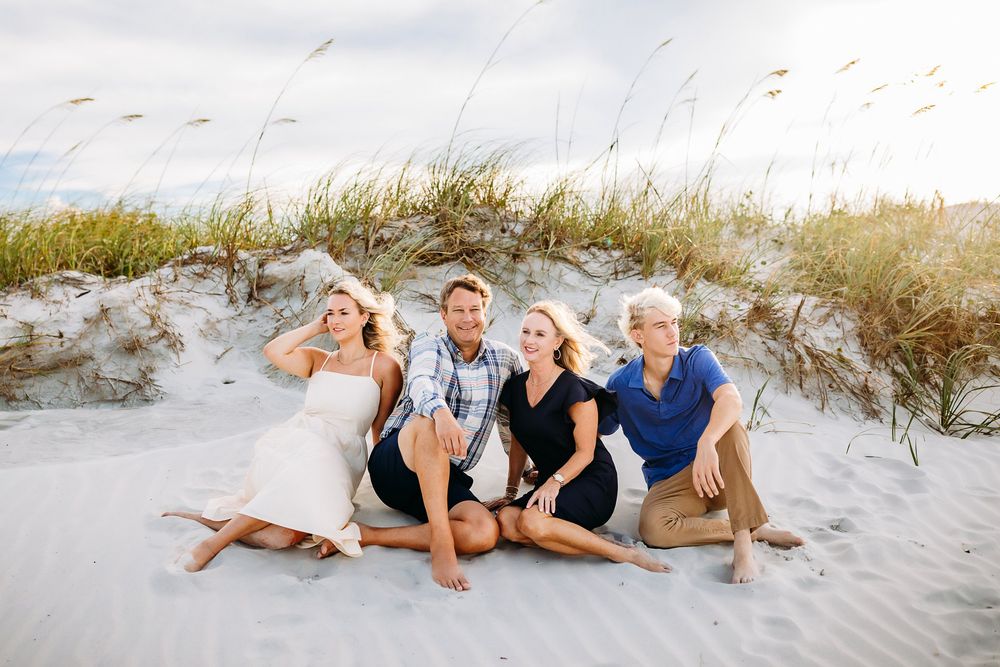Family photo session on a sandy beach with dunes and natural coastal vegetation in the background.