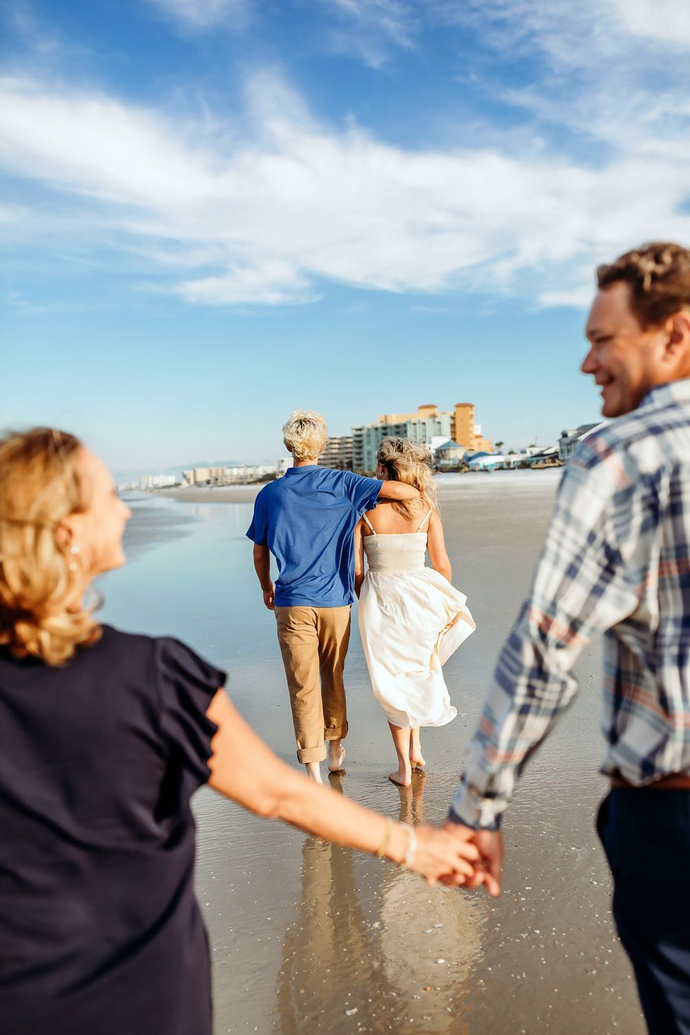 Family walking together holding hands along a sunny beach with blue skies and ocean views.