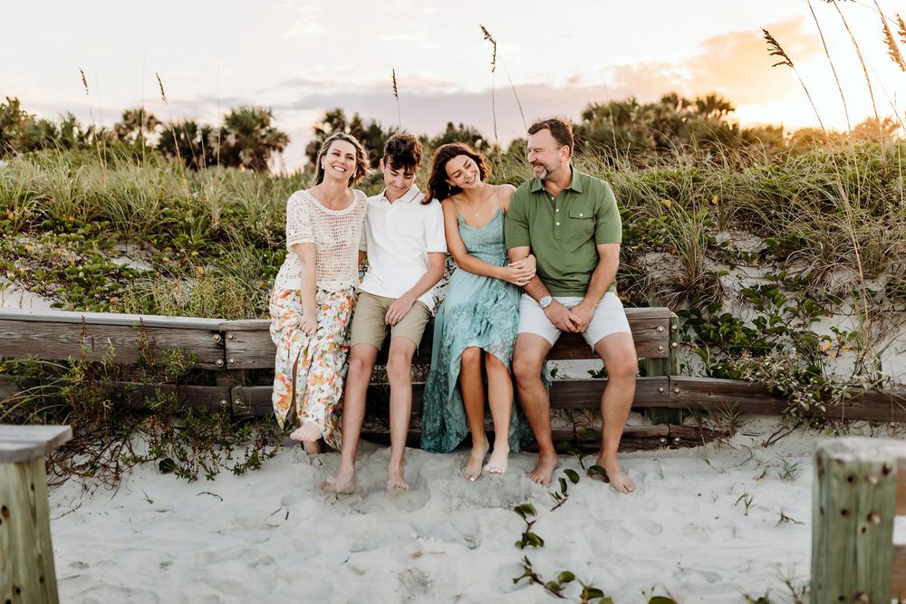 A family sits together on a fallen log at the beach during golden hour sunset.
