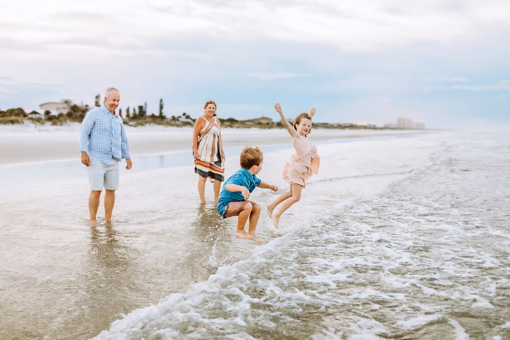 A family plays and splashes together in the shallow ocean waves at the beach on a sunny day.
