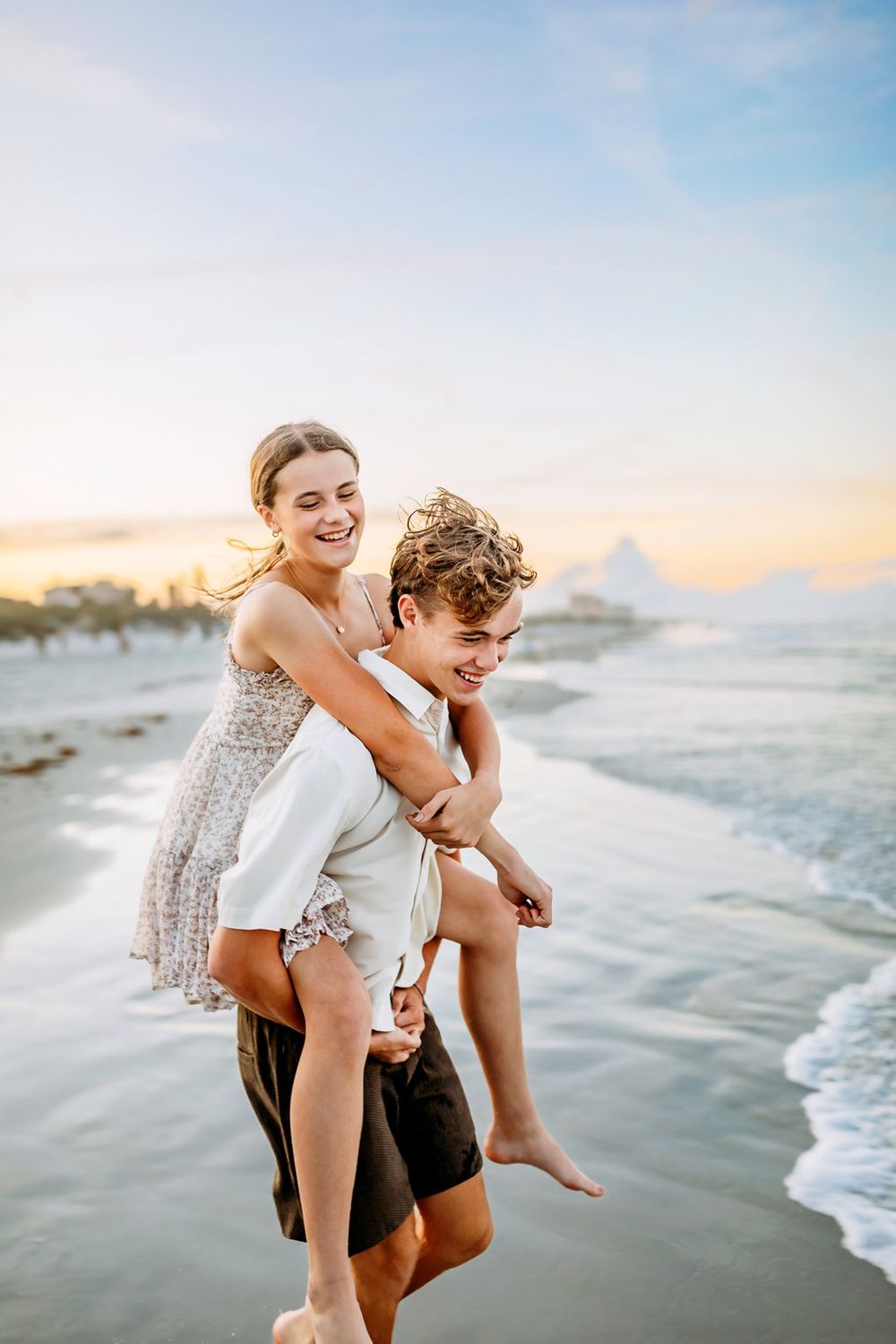 A couple plays and laughs together on a scenic beach at sunset with waves rolling in along the shoreline.